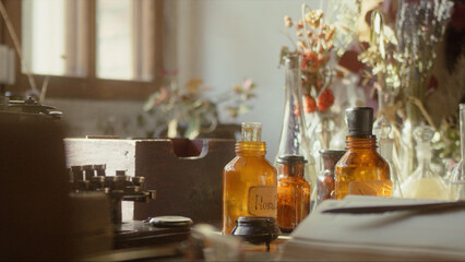 Obraz na płótnie Canvas Close-up of a perfumer's workplace. Vintage cinematic concept. Sunny day in the working workshop. Lots of ingredients, a book, glass flasks on the table. Depth of field
