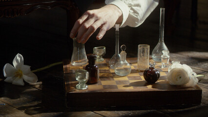 A man's hand plays chess with flasks on a chessboard. The concept of a perfumer, relaxation,...