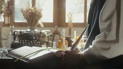 A man writer dips his pen into an inkwell and prepares to write a book in his workshop. Cosplay of the Middle Ages. Cinematic concept. Close-up feather