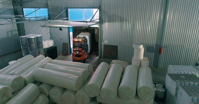 A forklift in a warehouse moves white bags. A forklift works in a warehouse. Rolls of padding polyester. Spunbond in rolls