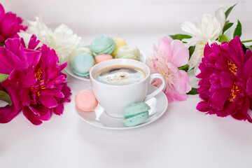 Fototapeta na wymiar Ideal morning breakfast -cup of coffee and macaroons on peonies flowers background