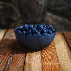 Still life. Fresh sweet blueberries in ceramic bowl standing on a wooden crate against gray stone background. Copy space