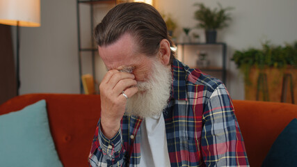 Upset disappointed senior grandfather man wipes tears and cries from despair, being sad because of...