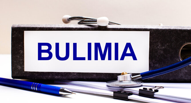 The desktop has a stethoscope, a blue pen, and a gray file folder with the text BULIMIA. Medical concept