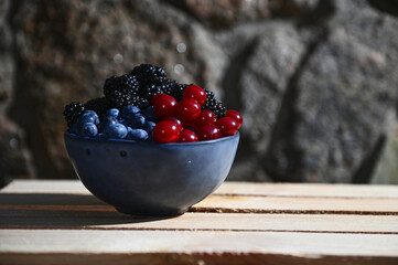 Close-up of seasonal wild organic berries- blueberries, blackberries and cherries in blue ceramic bowl on a wooden crate