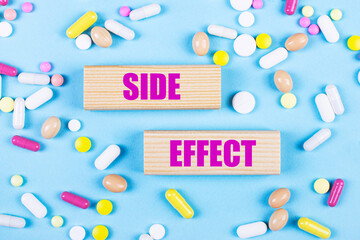 On a light blue background, multi-colored pills and wooden blocks with the text SIDE EFFECT. Pharmaceutics. Medical concept.