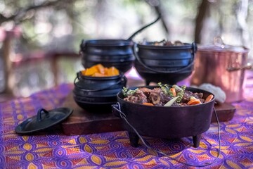 Closeup shot of tasty meat dishes on small metal pots on a purple table cloth