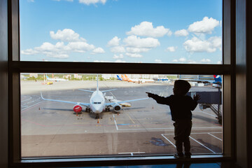 Moscow, Russia 07 14 22 Little boy carry bag waiting boarding to flight in airport transit hall and looking through the window at airplane departure. Active family lifestyle, travel by air with child 