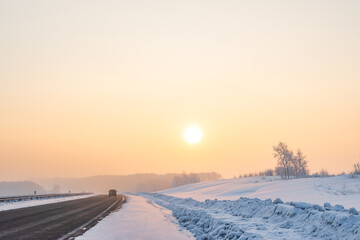 a view of a winter frosty landscape with an asphalt road, a car walking along it and a bright...