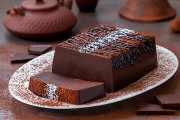 Sliced chocolate jelly pudding or mousse cake on a white plate with chocolate sauce and sprinkle of coconut flakes. Vegan dessert made from dark chocolate, cocoa, coconut milk and agar-agar.
