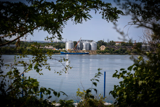 Industrial buildings and storage containers of the port of Giurgiu in Romania seen between branches of a trees on the other side of Danube river in the city of Ruse, Bulgaria