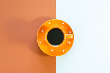 Coffee in an orange cup with white polka dots and saucer on a split white and orange background