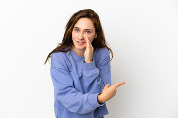 Young caucasian woman isolated on white background pointing to the side to present a product and whispering something