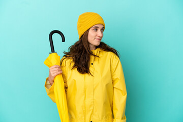 Young caucasian man holding an umbrella isolated on blue background looking side