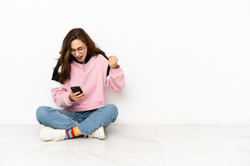 Young caucasian woman sitting on the floor isolated on white background surprised and sending a message