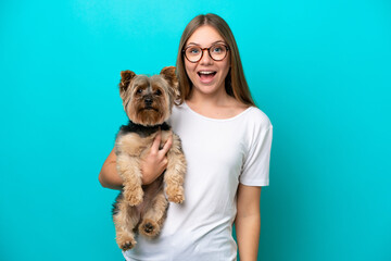 Young Lithuanian woman holding a dog isolated on blue background with surprise and shocked facial...