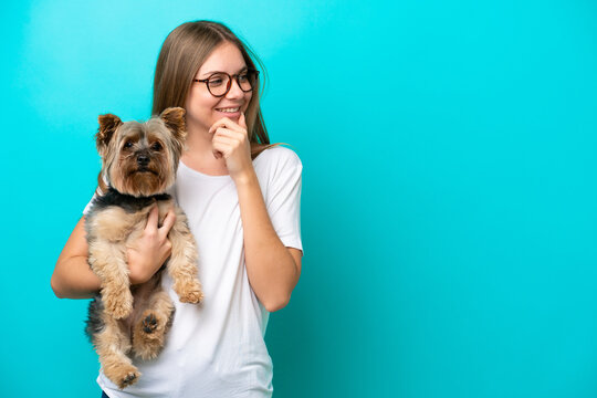 Young Lithuanian woman holding a dog isolated on blue background thinking an idea and looking side