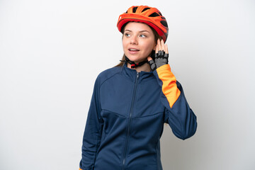Young cyclist Lithuanian woman isolated on white background listening to something by putting hand on the ear