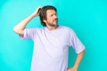 Senior dutch man isolated on blue background having doubts while scratching head