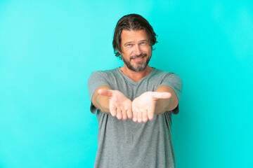 Senior dutch man isolated on blue background holding copyspace imaginary on the palm to insert an ad