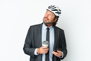 Business senior man with a bike helmet isolated on white background holding coffee to take away and a mobile while thinking something