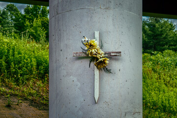A simple white wooden cross with flowers on a highway pillar is a memorial where a loved one passed...