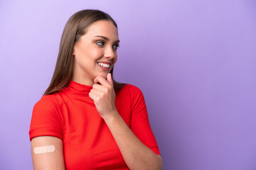 Young caucasian woman wearing band aid isolated on purple background thinking an idea and looking side