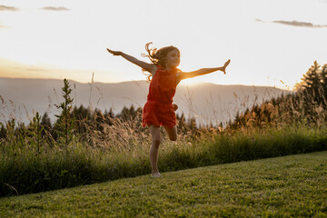 Fototapeta premium Mädchen, 8 Jahre, springt in einer Wiese bei Sonnenuntergang, Kärnten, Österreich