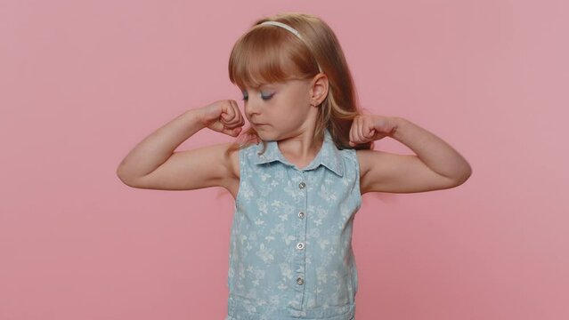 I am strong and independent. Fit sporty young preteen child girl kid showing biceps and looking confident, feeling power strength success win. Little toddler children alone on studio pink background