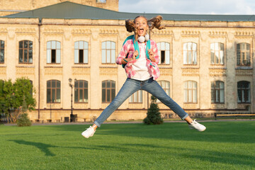 Happy energetic teen girl jumping in school yard outdoors, Knowledge day