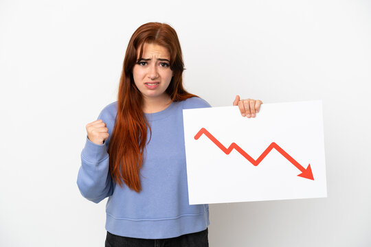 Young redhead woman isolated on white background holding a sign with a decreasing statistics arrow symbol and angry