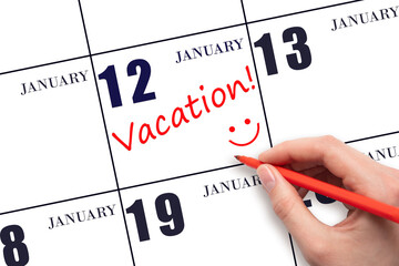 A hand writing a VACATION text and drawing a smiling face on a calendar date 12 January. Vacation...