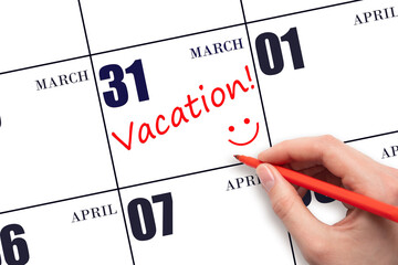 A hand writing a VACATION text and drawing a smiling face on a calendar date 31 March. Vacation...