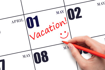 A hand writing a VACATION text and drawing a smiling face on a calendar date 1 May. Vacation...