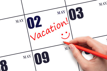 2nd day of May. A hand writing a VACATION text and drawing a smiling face on a calendar date 2 May....