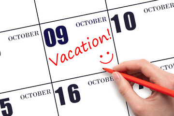 A hand writing a VACATION text and drawing a smiling face on a calendar date 9 October. Vacation...