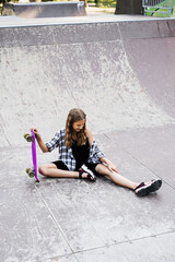 Active child girl after fall from penny board injured, sitting and looking at bruise on sport ramp on skate park playground.