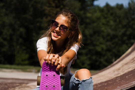 Happy smiling girl with skate board sitting on skate playground and having fun. Extreme sport lifestyle. Laughing child with skate board posing on sport ramp.