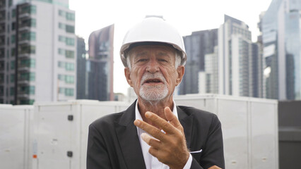 An old elderly engineer man or worker, people talking on webcam video call conference, working in industry factory. Chiller tower or cooling tower in building. System work machine pipe lines.