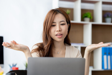 Beautiful Asian businesswoman sitting in her private office, she is talking to her partner via video call on her laptop, she is a female executive of a startup company. Concept of financial management