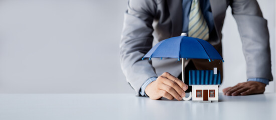 Individuals holding small umbrellas and model homes, housing insurance against impending loss and...