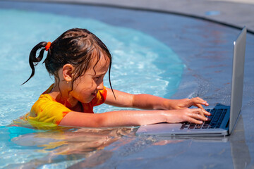 Beautiful young business girl using laptop and working online remotely in the swimming pool.