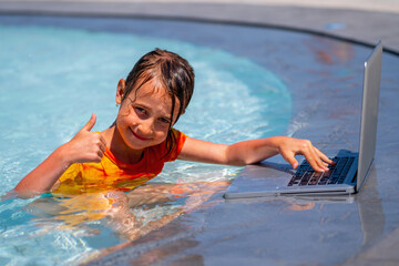 POrtrait of beautiful young girl gesturing thumb up, using laptop and working online remotely in the swimming pool. Summer vacations, rest and work at the same time.