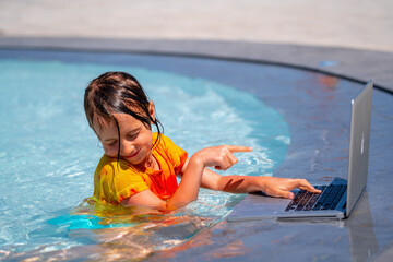 Beautiful girl using laptop online business remotely in the swimming pool. 