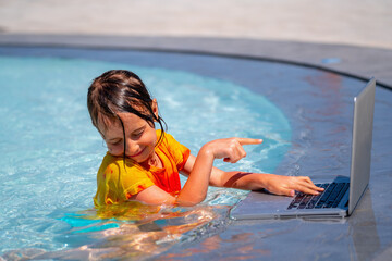 Funny facial expression of beautiful young girl using laptop in the swimming pool. She working online remotely.
