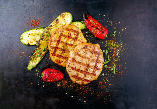 Traditionelle Putenschnitzel vom Grill in Curry Marinade mit gegrilltem Gem&uuml;se serviert als Draufsicht auf einem alten rustikalen Board mit Textfreiraum 