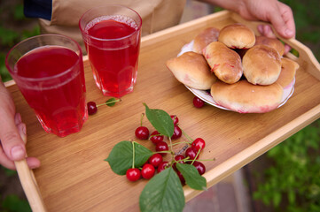 Top view of a housewife holding serving tray with homemade cherry pies and glasses with refreshing compote from cherries