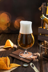 A beautiful tall glass with beer and foam on a wooden table. Delicious snacks. Organic products for home production.