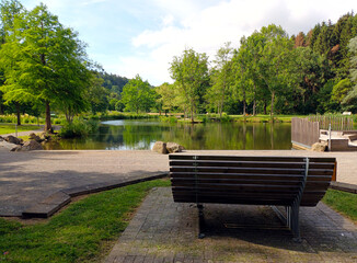 Fototapeta na wymiar Bank an romantischem Weiher im Kurpark Daun in der Eifel / Vulkaneifel, Rheinland-Pfalz. 