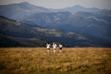 Fototapeta na wymiar Three Young Girls Running into the Beautiful Mountains